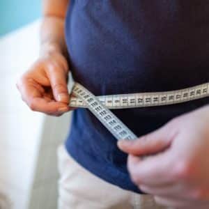 man measures her abdomen with a measuring tape